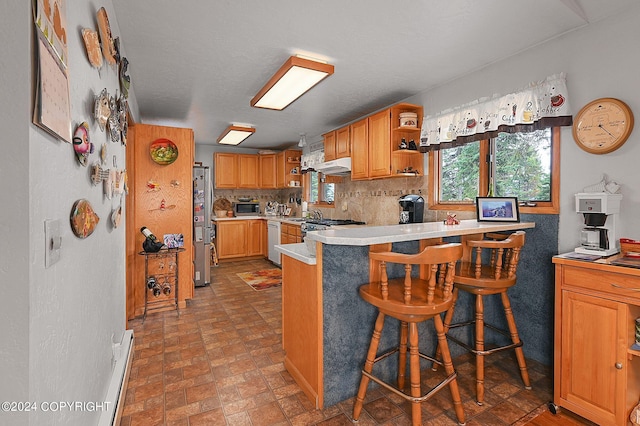 kitchen featuring a baseboard radiator, backsplash, kitchen peninsula, a kitchen breakfast bar, and stainless steel appliances