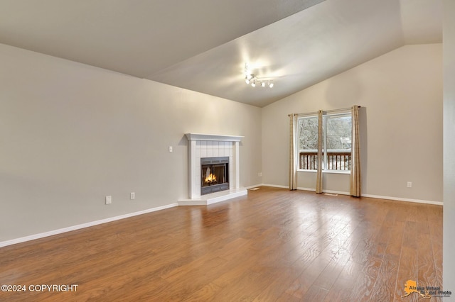 unfurnished living room with hardwood / wood-style floors, a tile fireplace, and vaulted ceiling