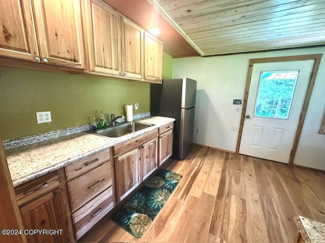 kitchen with light wood-type flooring, stainless steel refrigerator, sink, light stone countertops, and wood ceiling