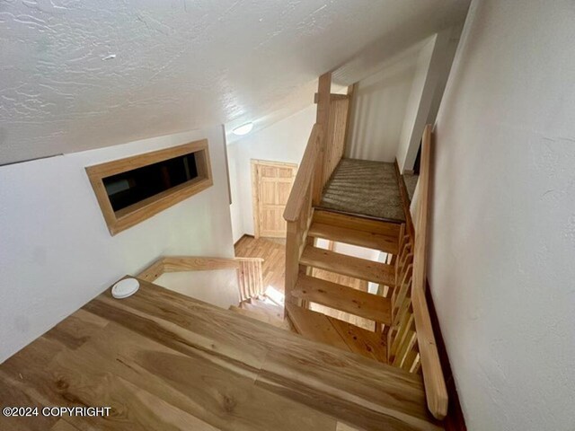 stairway with wood-type flooring, a textured ceiling, and vaulted ceiling