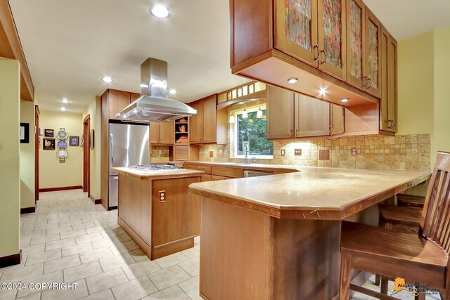 kitchen with island range hood, stainless steel fridge, a kitchen island, a kitchen bar, and kitchen peninsula