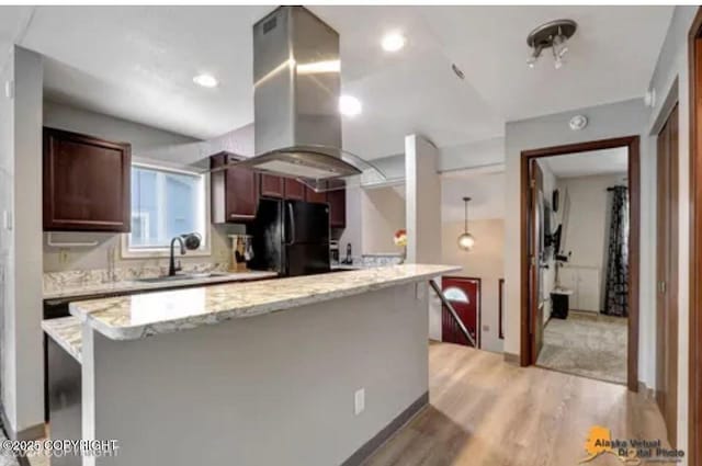 kitchen featuring light hardwood / wood-style floors, black fridge, sink, island range hood, and light stone counters