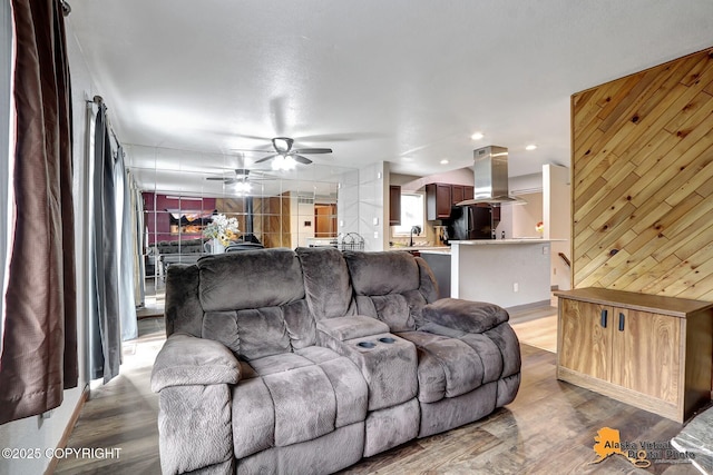 living room with ceiling fan, light hardwood / wood-style floors, and wood walls