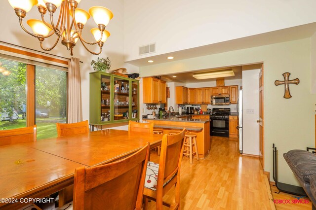 dining space featuring light hardwood / wood-style flooring, a high ceiling, sink, and a chandelier