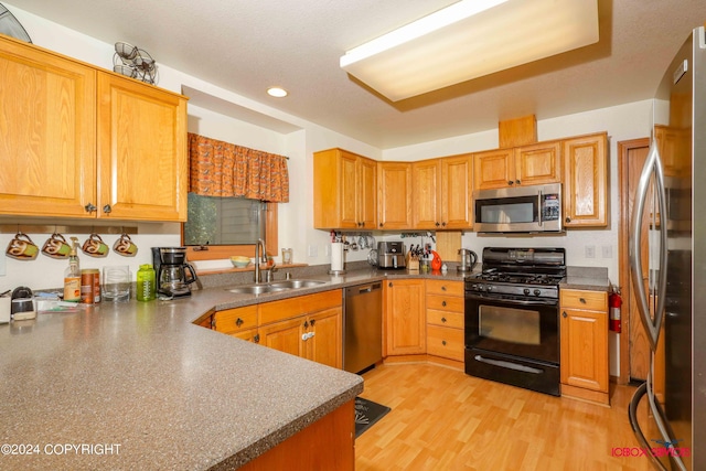 kitchen with appliances with stainless steel finishes, brown cabinetry, a sink, and light wood-style floors