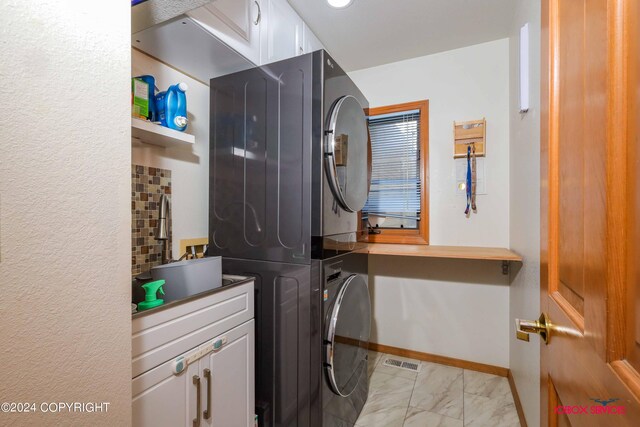 laundry room featuring cabinets, light tile patterned floors, and stacked washing maching and dryer