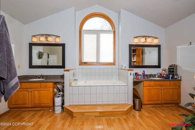 bathroom featuring hardwood / wood-style flooring, a relaxing tiled tub, and vaulted ceiling