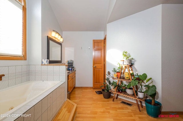 full bath featuring visible vents, vanity, a bath, and wood finished floors