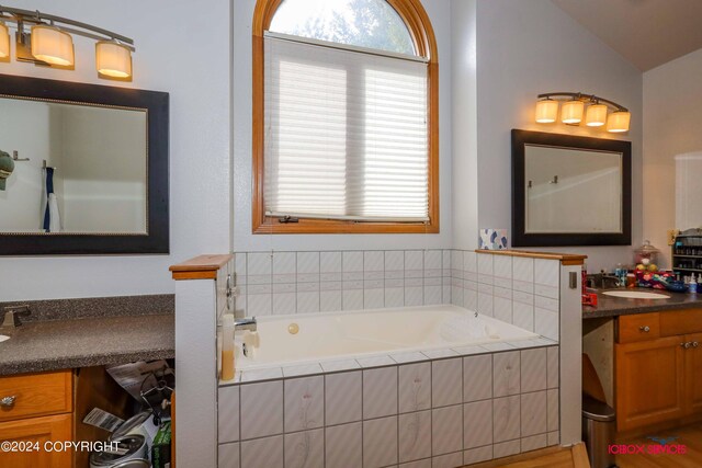 bathroom featuring vanity, vaulted ceiling, a relaxing tiled tub, and hardwood / wood-style flooring