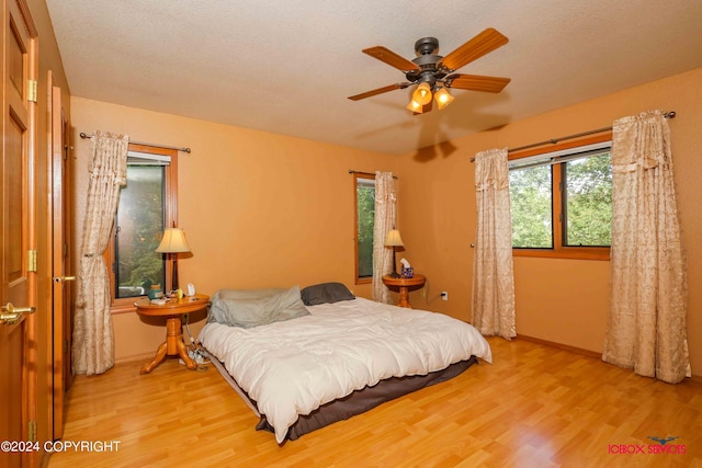 bedroom featuring a ceiling fan, a textured ceiling, baseboards, and wood finished floors