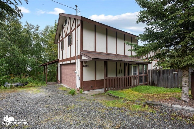 tudor house featuring an attached garage, covered porch, brick siding, fence, and gravel driveway