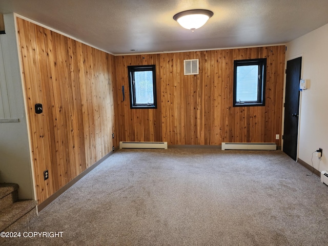 unfurnished room featuring carpet, a textured ceiling, a baseboard heating unit, and wood walls