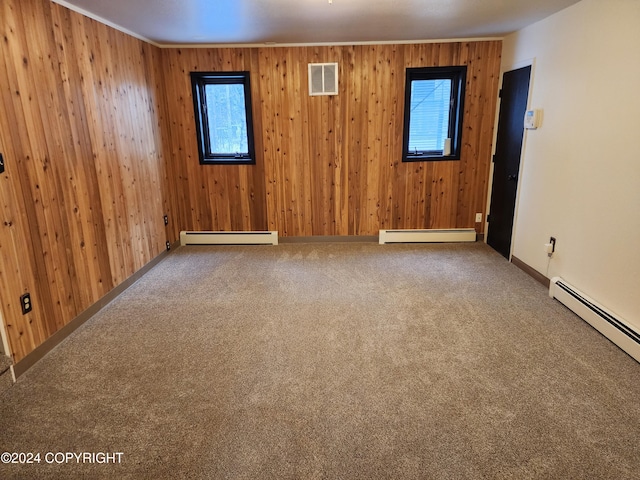 carpeted empty room with ornamental molding, a baseboard heating unit, and wood walls