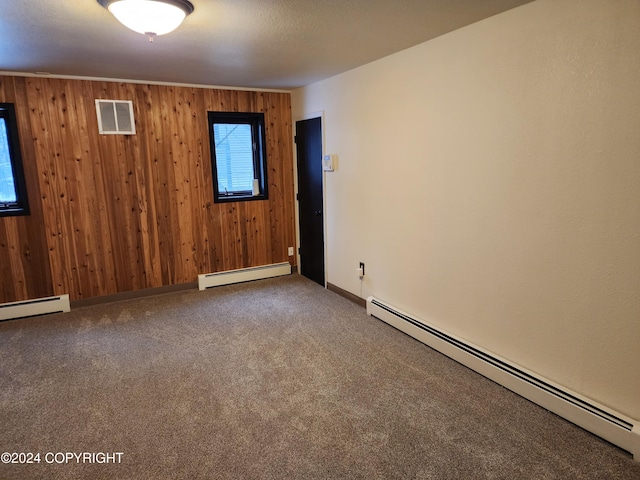 empty room with carpet floors, baseboard heating, and wooden walls