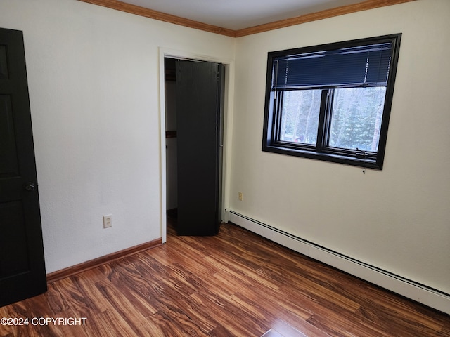 empty room with hardwood / wood-style floors, ornamental molding, and a baseboard heating unit