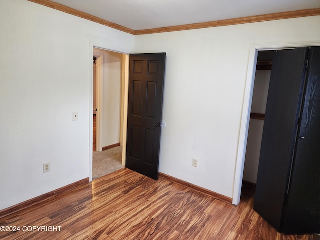 unfurnished bedroom with hardwood / wood-style floors, ornamental molding, and a closet