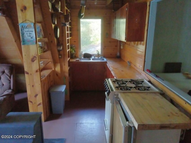 kitchen with butcher block countertops, a sink, white gas stove, and wood walls