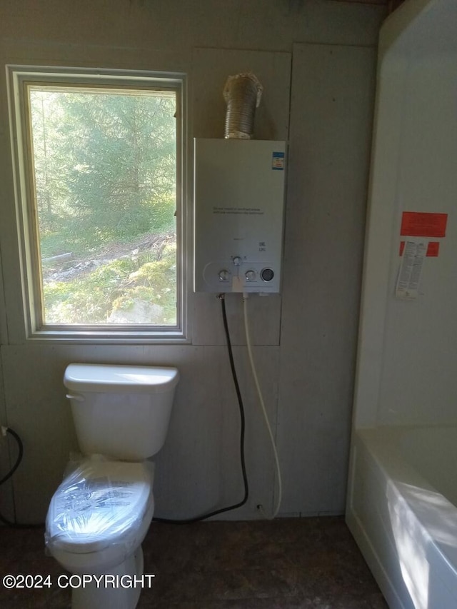 bathroom featuring a tub to relax in, toilet, and tankless water heater