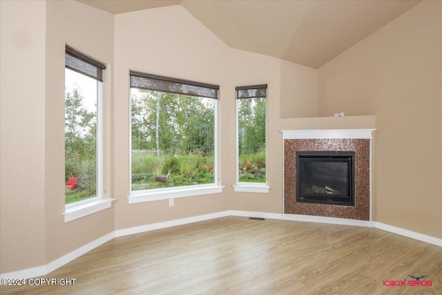 unfurnished living room featuring a wealth of natural light, wood-type flooring, a tile fireplace, and vaulted ceiling