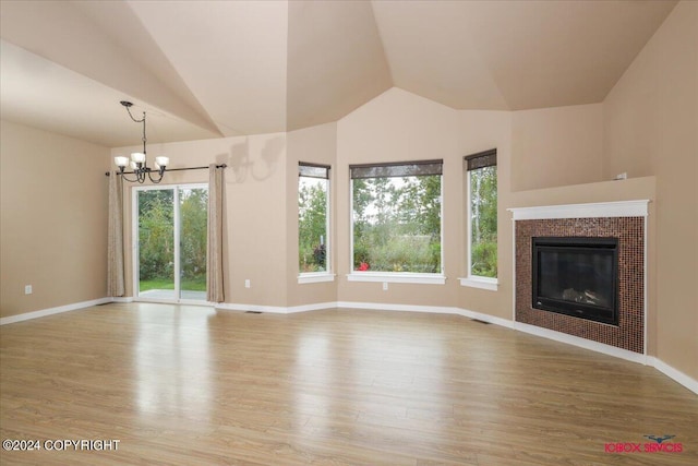 unfurnished living room featuring a tiled fireplace, lofted ceiling, light hardwood / wood-style flooring, and an inviting chandelier