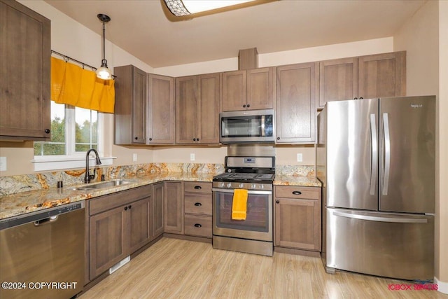 kitchen featuring hanging light fixtures, stainless steel appliances, sink, light stone counters, and light wood-type flooring