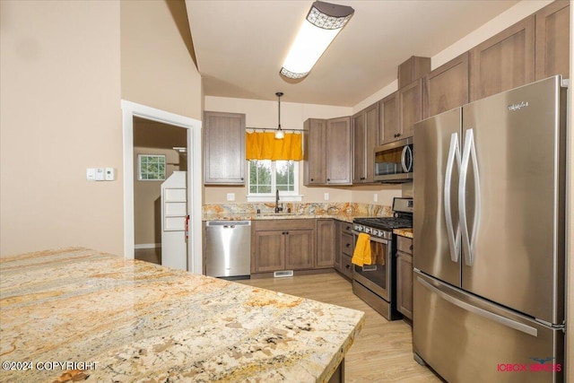 kitchen featuring light hardwood / wood-style flooring, hanging light fixtures, stainless steel appliances, sink, and light stone counters