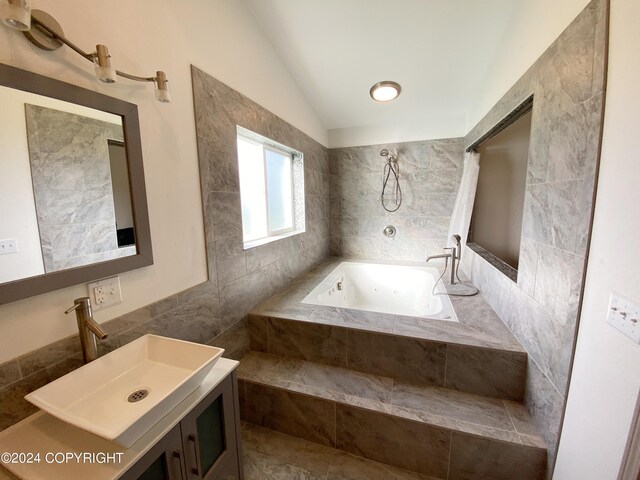 bathroom with tile walls, vaulted ceiling, tiled bath, and vanity