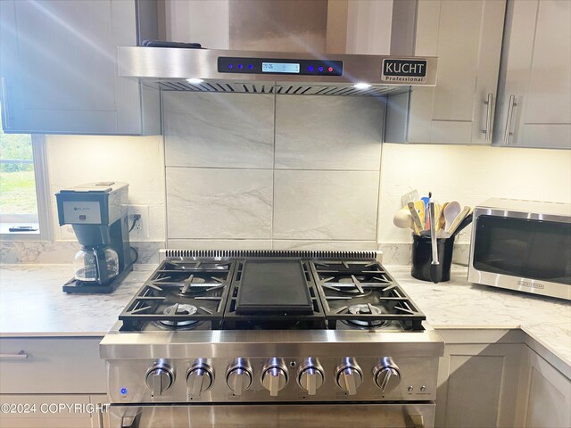 kitchen with gray cabinetry, light stone countertops, range hood, and stainless steel appliances