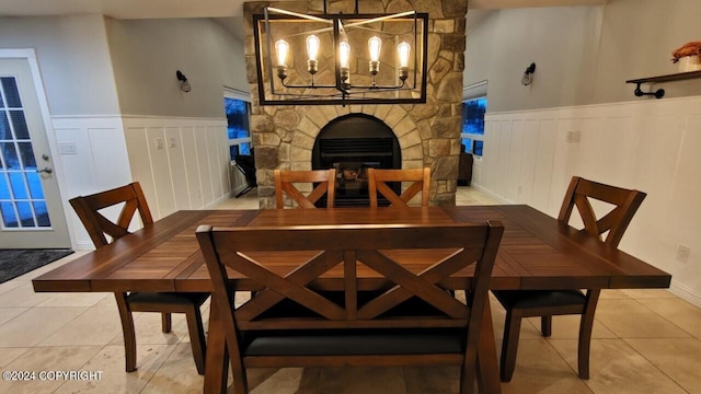 dining room with wainscoting, a notable chandelier, a stone fireplace, and tile patterned floors