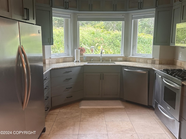 kitchen with light tile patterned floors, appliances with stainless steel finishes, light stone counters, gray cabinetry, and a sink