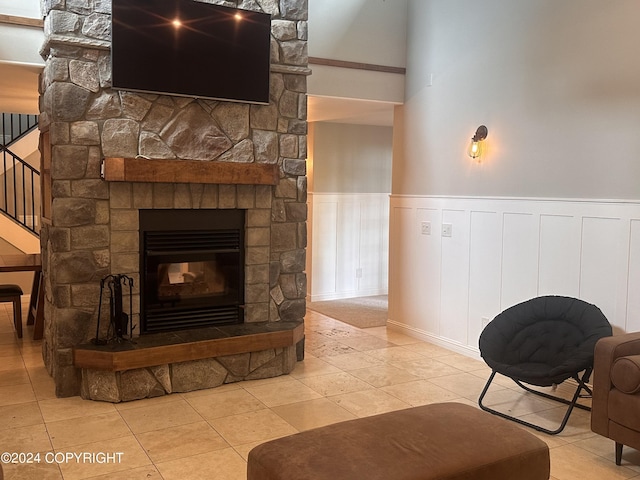 tiled living room featuring a wainscoted wall, a stone fireplace, and stairs