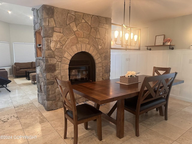 dining area with a wainscoted wall, a fireplace, a decorative wall, and an inviting chandelier