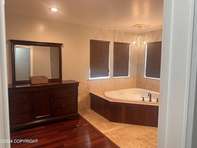 bathroom with a garden tub, recessed lighting, a notable chandelier, wood finished floors, and vanity