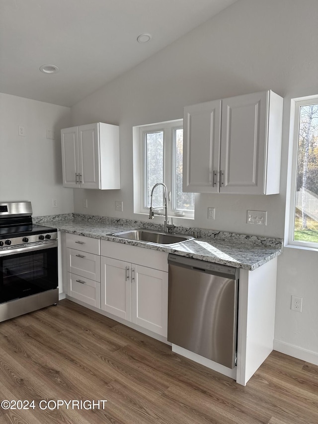 kitchen with appliances with stainless steel finishes, white cabinets, a sink, and light wood-style flooring