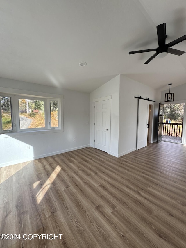 interior space with ceiling fan, a barn door, wood finished floors, baseboards, and vaulted ceiling