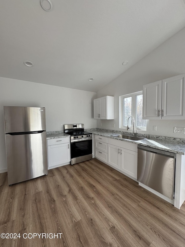 kitchen featuring lofted ceiling, appliances with stainless steel finishes, white cabinetry, a sink, and wood finished floors