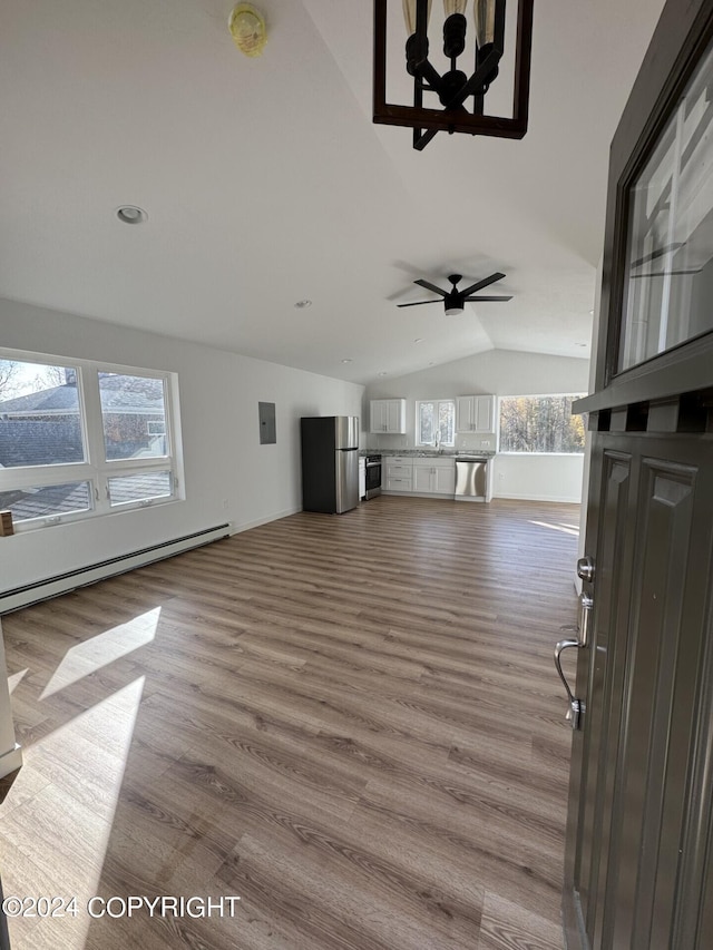 unfurnished living room with a baseboard heating unit, vaulted ceiling, a sink, wood finished floors, and electric panel