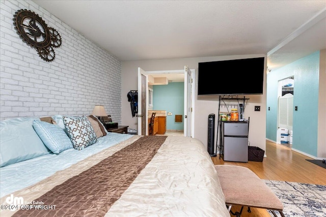 bedroom with light hardwood / wood-style floors, brick wall, and stainless steel refrigerator