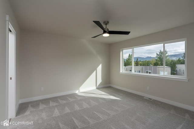 carpeted spare room with a mountain view, baseboards, and a ceiling fan