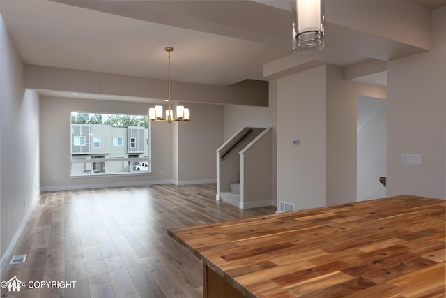 unfurnished dining area with visible vents, baseboards, stairway, an inviting chandelier, and wood finished floors