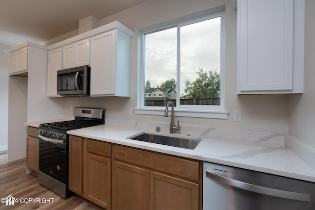 kitchen with light stone counters, light wood-style flooring, appliances with stainless steel finishes, white cabinets, and a sink