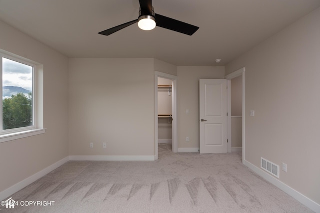 unfurnished bedroom with visible vents, a walk in closet, baseboards, carpet flooring, and a ceiling fan