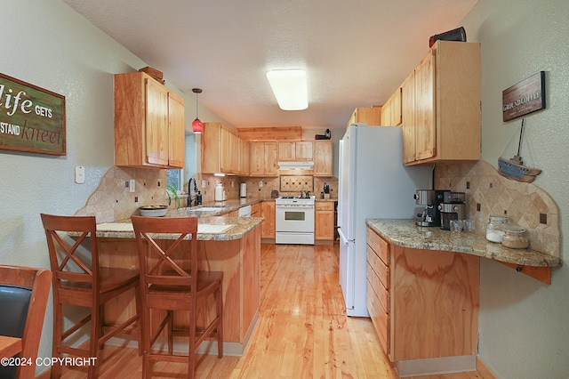 kitchen with a kitchen bar, kitchen peninsula, decorative light fixtures, and white appliances