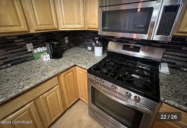 kitchen featuring stainless steel appliances, light stone countertops, backsplash, and light brown cabinetry