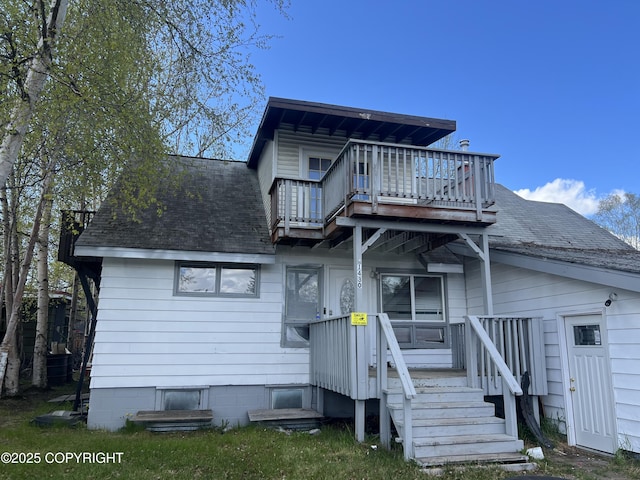 rear view of property featuring a shingled roof and a balcony