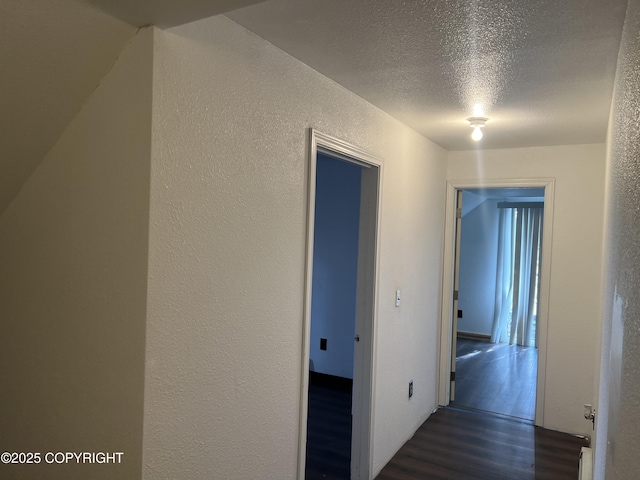 corridor with a textured wall, dark wood-style floors, and a textured ceiling