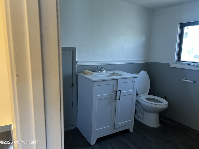 half bath with wood finished floors, toilet, and vanity
