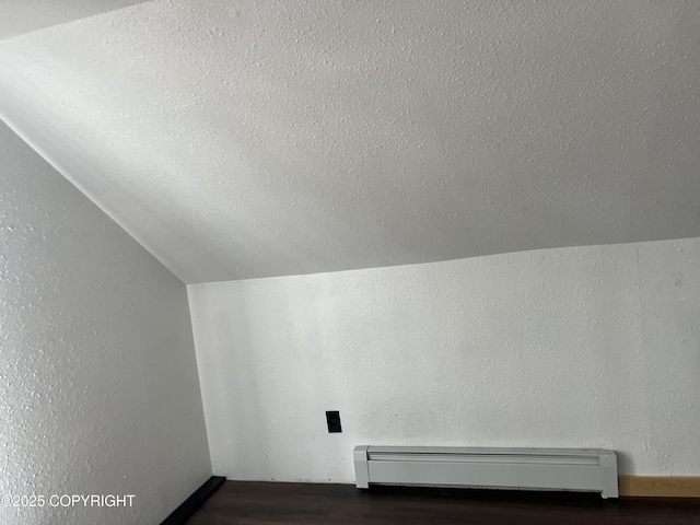 additional living space with a baseboard heating unit, vaulted ceiling, wood finished floors, and a textured ceiling