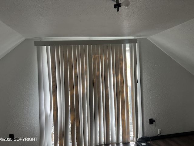bonus room with lofted ceiling, a textured ceiling, a textured wall, and wood finished floors