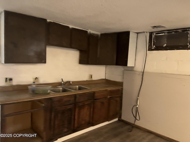 kitchen with a sink, dark brown cabinetry, dark wood-type flooring, and dark countertops